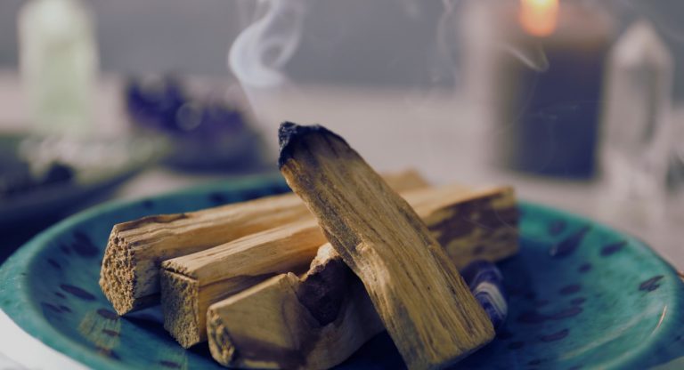 Bâtons de palo santo fumants posés sur une assiette en céramique turquoise