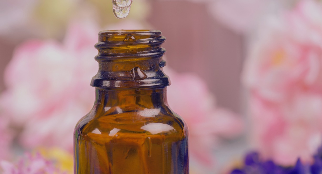 Flacon ambré d'élixir floral avec compte-gouttes devant des fleurs roses
