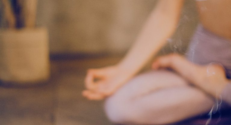 Personne assise en tailleur en méditation avec de l'encens fumant