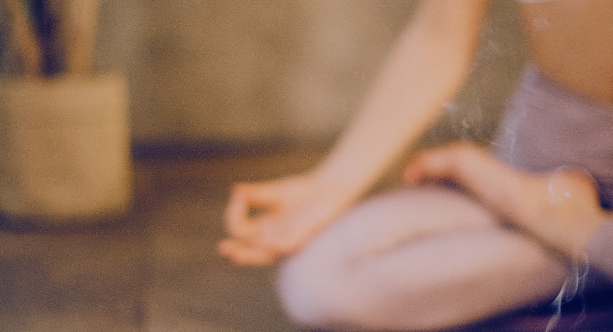 Personne assise en tailleur en méditation avec de l'encens fumant