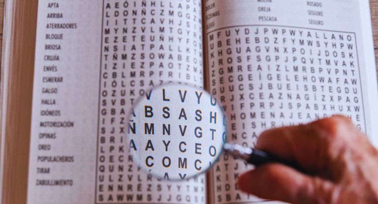 Main tenant une loupe au-dessus d'une grille de mots à trouver