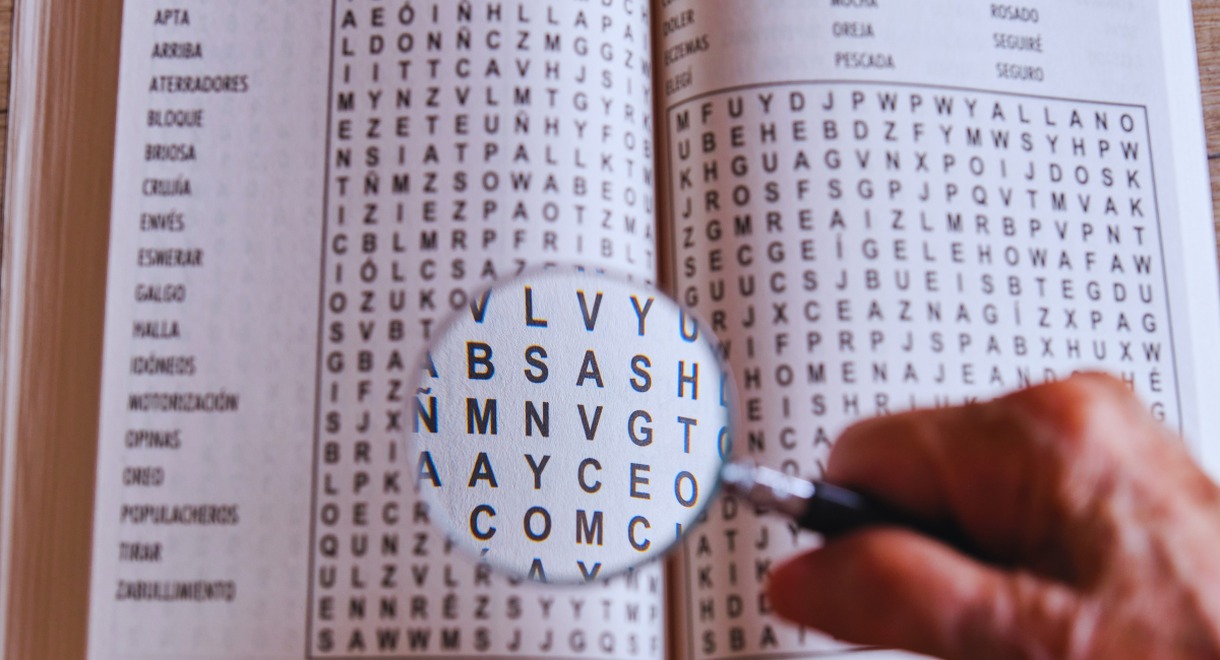 Main tenant une loupe au-dessus d'une grille de mots à trouver