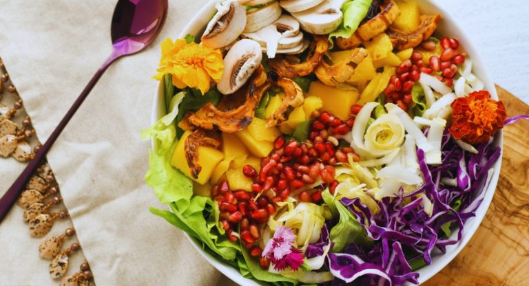 Bol de salade colorée avec légumes frais, grenade et fleurs comestibles