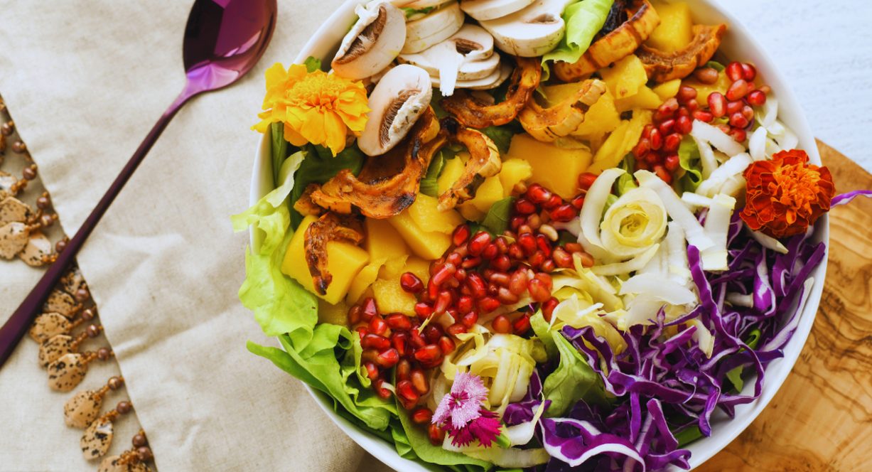 Bol de salade colorée avec légumes frais, grenade et fleurs comestibles